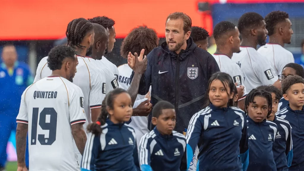 Harry Kane in a navy England tracksuit top with the Three Lions crest, applauding as he lines up with teammates and child mascots before England's match against Panama at the 2026 World Cup.